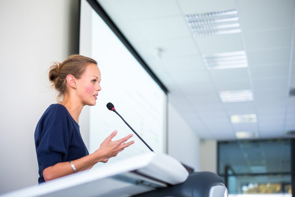 A diverse audience enthusiastically claps during a presentation, showcasing engagement and support in a well-lit modern venue.