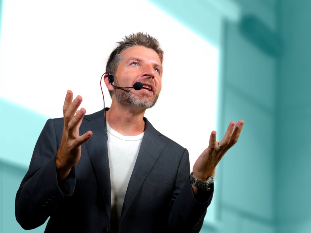 Business presenter in a suit passionately gestures while speaking into a headset, emphasizing key points during a conference or seminar.
